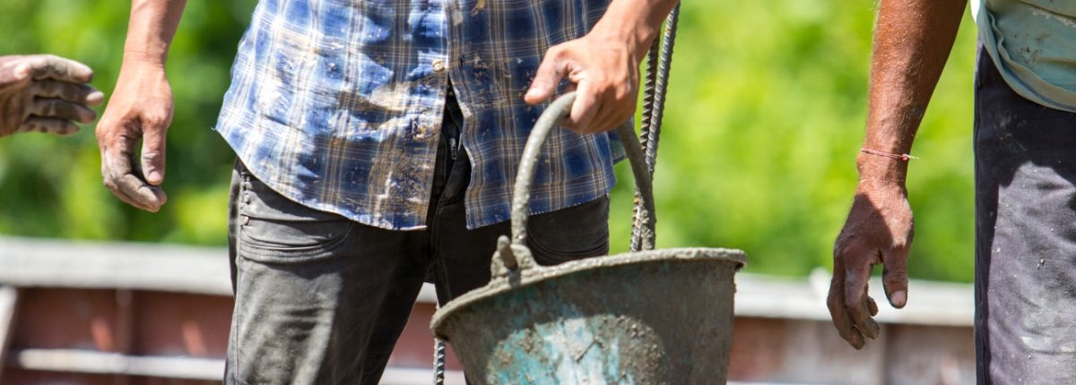 men walking with a dirt-covered bucket
